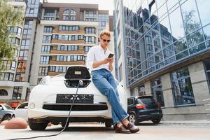 uomo Tenere energia ricarica cavo per elettrico auto nel all'aperto auto parco. e lui S andando per Collegare il auto per il ricarica stazione nel il parcheggio lotto vicino il shopping centro foto