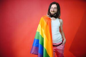 bello giovane uomo con orgoglio movimento lgbt arcobaleno bandiera su spalla contro bianca sfondo. uomo con un' gay orgoglio bandiera. foto