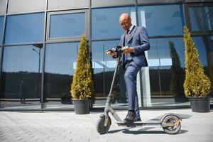 uomo d'affari con elettrico scooter in piedi nel davanti di moderno attività commerciale edificio parlando su Telefono. foto