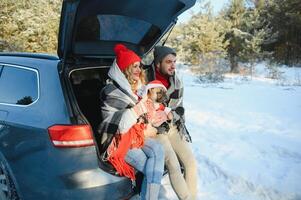 coppia tipo e ragazza seduta nel auto giocando con cane nel inverno foresta foto