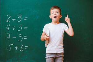 indietro per scuola concetto. scuola bambino nel classe. contento ragazzo contro verde lavagna. inteligente bambino nel aula. idea e formazione scolastica concetto foto