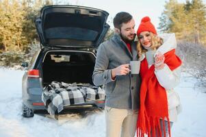 coppia nel amore seduta nel auto tronco potabile caldo tè nel nevoso inverno foresta e chattare. persone rilassante all'aperto durante strada viaggio. san valentino giorno foto