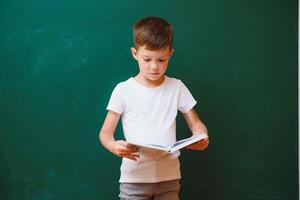 indietro per scuola concetto. scuola bambino nel classe. contento ragazzo contro verde lavagna. inteligente bambino nel aula. idea e formazione scolastica concetto foto