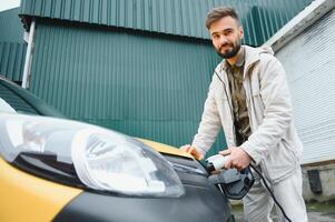 uomo Tenere energia ricarica cavo per elettrico auto nel all'aperto auto parco. e lui S andando per Collegare il auto per il ricarica stazione nel il parcheggio lotto vicino il shopping centro foto