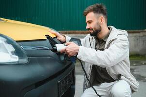 uomo Tenere energia ricarica cavo per elettrico auto nel all'aperto auto parco. e lui S andando per Collegare il auto per il ricarica stazione nel il parcheggio lotto vicino il shopping centro foto