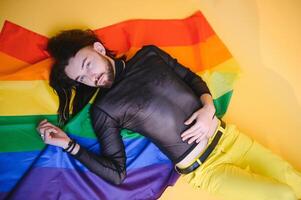bello giovane uomo con orgoglio movimento lgbt arcobaleno bandiera su spalla contro bianca sfondo. uomo con un' gay orgoglio bandiera. foto