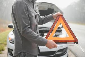 giovane irritato casuale uomo provando per fix il suo rotto auto all'aperto. uomo in attesa per rimorchio servizio per Aiuto auto incidente su il strada. ciglio della strada assistenza concetto. foto