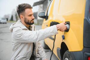 contento giovane adulto uomo ricarica automobile batteria a partire dal piccolo pubblico stazione. foto