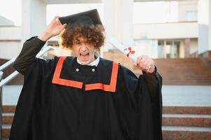 eccitato diplomato alunno nel toga con aumentato mani Tenere diploma. foto