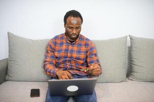giovane africano uomo Tenere credito carta e tavoletta a casa foto