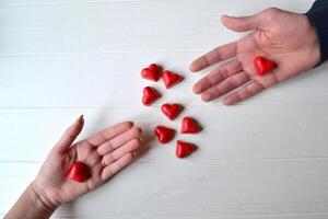 rosso caramelle nel un' modulo di cuore su il tavolo. mani di coppia nel amore. sfondo per saluto carta su un' San Valentino giorno. foto