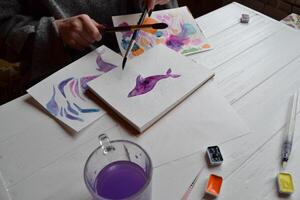 donna vernici nel un' album da disegno. utensili per pittura su il bianca di legno scrivania. pittore opera. foto