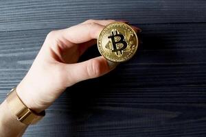bitcoin oro moneta nel femmina mano su il buio blu di legno sfondo. foto