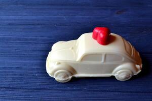 bianca cioccolato nel un' modulo di auto con rosso caramella nel un' modulo di cuore su il buio blu di legno tavolo. foto