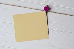 giallo promemoria foglio fissato con un' decorativo perno su un' bianca di legno tavola. foto