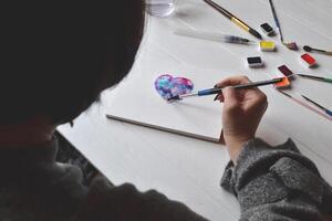 donna vernici nel un' album da disegno. utensili per pittura su il bianca di legno scrivania. pittore opera. foto