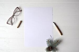 il foglio di bianca carta con penna, occhiali e ramo di sempreverde su il di legno scrivania. foto