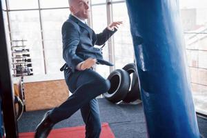 un uomo d'affari calvo arrabbiato batte una pera da boxe in palestra. concetto di gestione della rabbia foto