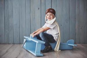 bambino felice in cappello pilota che gioca con l'aeroplano di legno contro. infanzia. fantasia, immaginazione. vacanza foto