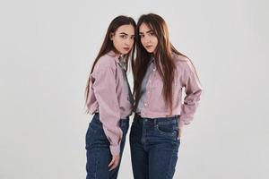 sempre insieme. due sorelle gemelle in piedi e in posa in studio con sfondo bianco foto