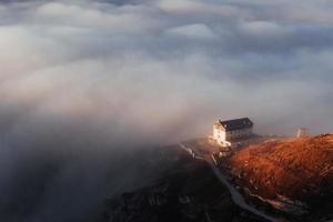 casa solitaria tra le nuvole in piedi sulla montagna che riceve una bella luce solare foto