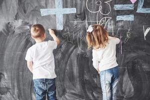 simpatica bambina e ragazzo che disegnano con i pastelli a cera sul muro. opere di bambino. carino allievo che scrive sulla lavagna foto