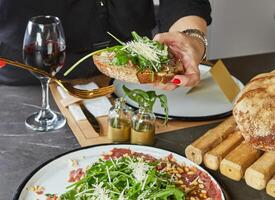 un' elegante hostess nel un' moderno cucina elegantemente posti un' delizioso piatto di carpaccio su pane su un' pulito marmo controsoffitto, dimostrando il arte di presentazione e culinario abilità foto