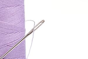 macro matassa di filo viola colori con un' ago su un' bianca sfondo foto