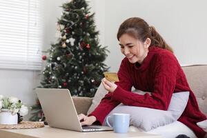 in linea acquisti. donna acquisto il computer portatile utilizzando credito carta seduta su divano a casa foto