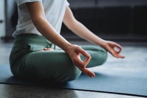 un' giovane ragazza si siede nel il loto posizione di sua mano su sua giro, sua dita piegato in il rango di mudra. tempo di zen, immersione verso l'interno, solitudine, solo a casa, la tranquillità e pace. foto