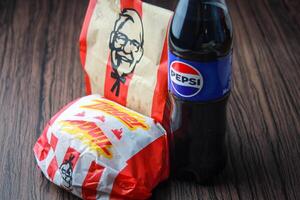 bangkok, Tailandia - marzo 3, 2024 - kfc pollo zenzero hamburger e fresco patatine fritte con pepsi bibita posto su un' nero di legno tavolo, porta via cibo, Rifiuto cibo, kfc fritte pollo, pepsi nuovo logo. foto