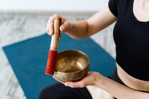 tibetano ciotola avvicinamento. il ragazza colpi il ciotola estrazione il suono per meditazione. pratica silenzio e rilassamento di il corpo a casa. foto