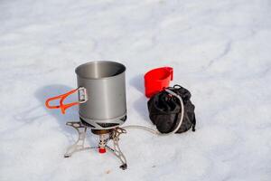 giocatore di bowling turista utensili In piedi nel il neve, gas bruciatore su un' escursione, un' impostato di attrezzatura per cucinando nel natura, ultra leggero impostato di attrezzatura, estremo viaggio foto