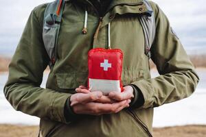 il tipo detiene nel il suo mani un' escursioni a piedi Borsa, un' primo aiuto kit con medicinali, un' rosso emergenza Borsa di primo aiuto. medicinali nel un' pacchetto, rosso attraversare. foto