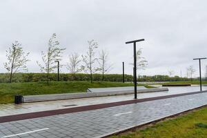 bicicletta sentiero nel il città parco, panchina per rilassamento, paesaggio design di urbano spazio posto per a passeggio, falciato prato verde erba, lampione progettista foto