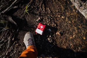 il primo aiuto kit abbattere per il terra, il uomo perso un' rosso Borsa con un' attraverso, un' piede nel un' scarpa, un' turista avuto perso nel il foresta, primo aiuto per il vittima. foto