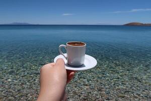 tradizionale Turco caffè tazza con modelli. donna mano Tenere il tazza su un' soleggiato estate giorno, esotico mare sfondo foto