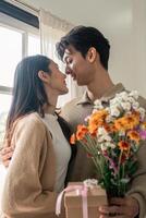 romantico giovane asiatico coppia Abbracciare una persona con Tenere fiori e sorridente nel vivente camera a casa. autunno nel amore. San Valentino concetto foto