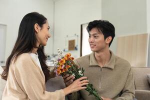 asiatico bello uomo mostrare il amore e dare fiori per il suo fidanzata nel vivente camera su San Valentino giorno. stile di vita concetto foto