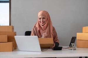 musulmano donne vendita in linea a casa con scatola. vendita in linea con scatola per accettare ordine a partire dal cliente. pmi attività commerciale idea. pacco consegna. musulmano donna Lavorando smartphone e il computer portatile a casa foto