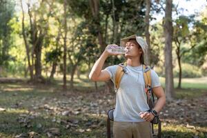 viaggiatore escursioni a piedi uomo trasporto un' zaino su il indietro e a piedi nel nazionale parco. uomo asiatico è riposo di bevanda acqua foto