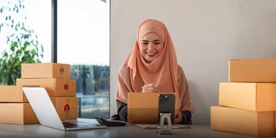 musulmano donne vendita in linea a casa con scatola. vendita in linea con scatola per accettare ordine a partire dal cliente. pmi attività commerciale idea. pacco consegna. musulmano donna Lavorando smartphone e il computer portatile a casa foto