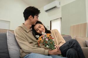 romantico giovane asiatico coppia Abbracciare una persona con Tenere fiori e sorridente nel vivente camera a casa. autunno nel amore. San Valentino concetto foto