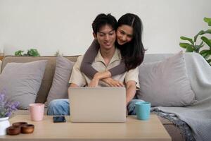 contento coppia asiatico sedersi rilassare su divano nel vivente camera Guardando video su il computer portatile insieme a casa foto