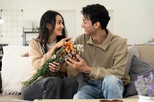 asiatico bello uomo mostrare il amore e dare fiori per il suo fidanzata nel vivente camera su San Valentino giorno. stile di vita concetto foto