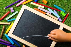 vista dall'alto della mini lavagna e dei colori su sfondo di erba di plastica. concetto di ritorno a scuola foto