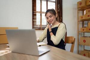 avviare pmi piccolo attività commerciale imprenditore pmi o libero professionista asiatico donna utilizzando un' il computer portatile con scatola, giovane successo asiatico donna in linea marketing pacchetto scatola e consegna concetto foto