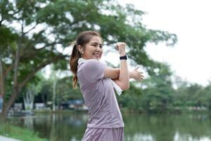 donna asiatico fare allungare esercizio allungare sua braccio, femmina allungare per riscaldamento su prima in esecuzione o allenarsi nel il parco foto