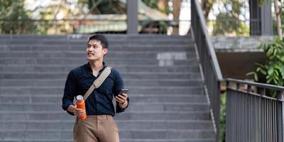 sorridente asiatico uomo d'affari a piedi per opera mentre per hold riutilizzabile eco amichevole ecologico tazza nel il città foto