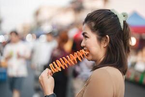 contento giovane asiatico viaggiatore buongustaio donna godere mangiare tornado patate patatine fritte a all'aperto notte mercato strada cibo foto